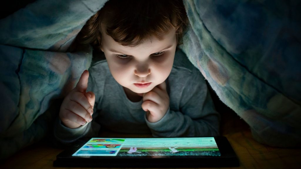 Enfant regarde tablette sous des couvertures 